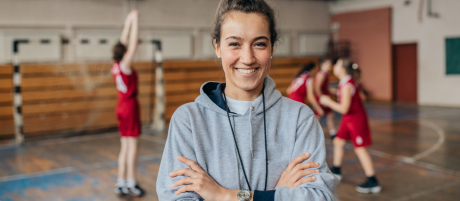 Portrait einer jungen Frau in einer Sporthalle, hinter ihr sieht man junge Menschen in Sportkleidung | Sparkasse Hannover