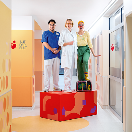 Ein Pfleger, eine Ärztin und eine Clownin stehen auf einem roten Podest | Sparkasse Hannover