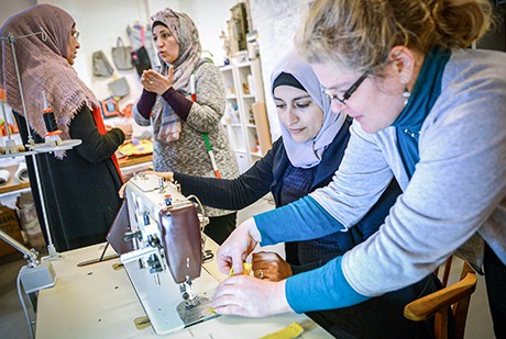 Eine Gruppe Frauen in einer Nähwerkstatt. Zwei Frauen mit Kopftuch sind im Gespräch. Eine Frau mit locken und Brille und eine weitere Frau mit Kopftuch erbeiten an einer Nähmaschine. | Sparkasse Hannover