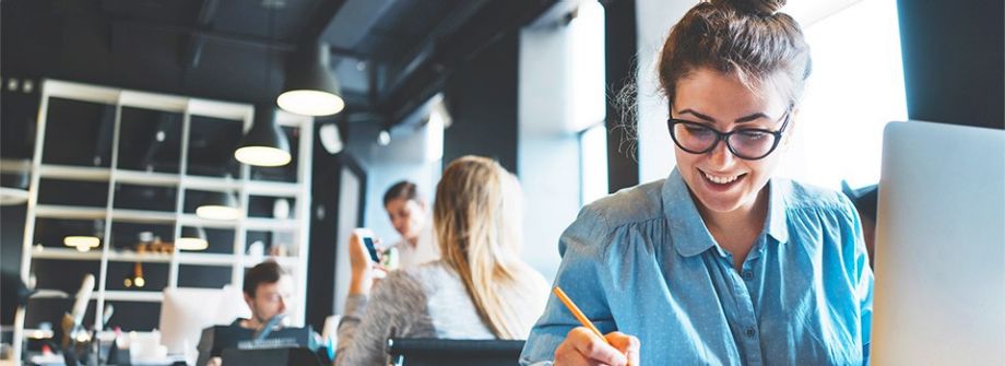 Junge Leute: Berufseinsteiger -  Nahaufnahme einer jungen Frau mit Brille, die an einem Laptop sitzt und Notizen aufschreibt | Sparkasse Hannover