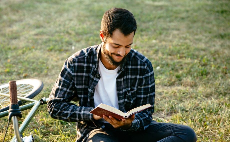 Junge Leute: Junger Mann sitzt im Gras und liest ein Buch | Sparkasse Hannover