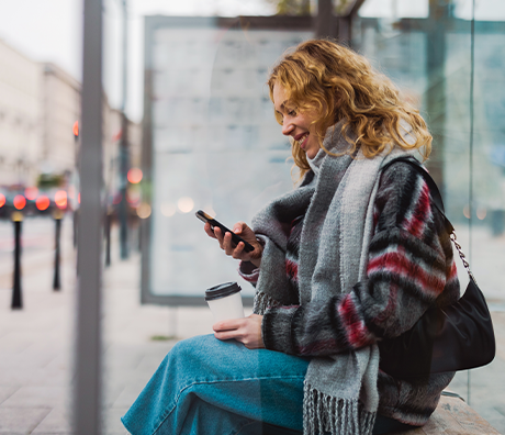Junge Frau sitzt mit dem Smartphone in der Hand an der Bushaltestelle | Sparkasse Hannover