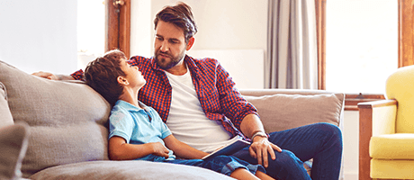Junge Leute: Ein Vater sitzt mit seinem Sohn auf der Couch und unterhält sich mit ihm | Sparkasse Hannover