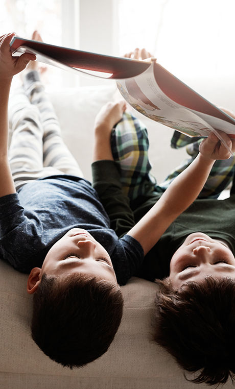 Junge Leute: Zwei Jungen liegen auf einem Sofa und schauen sich mit gestreckten Armen ein Buch an | Sparkasse Hannover