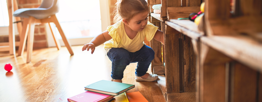 Junge Leute: Kleines Mädchen greift in ein Regal , davor liegen Bücher auf dem Boden | Sparkasse Hannover