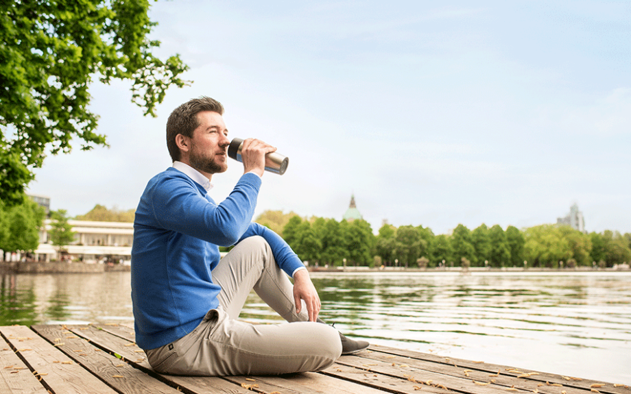  Ein Mann sitzt entspannt auf einem Steg am Wasser und trinkt etwas | Sparkasse Hannover